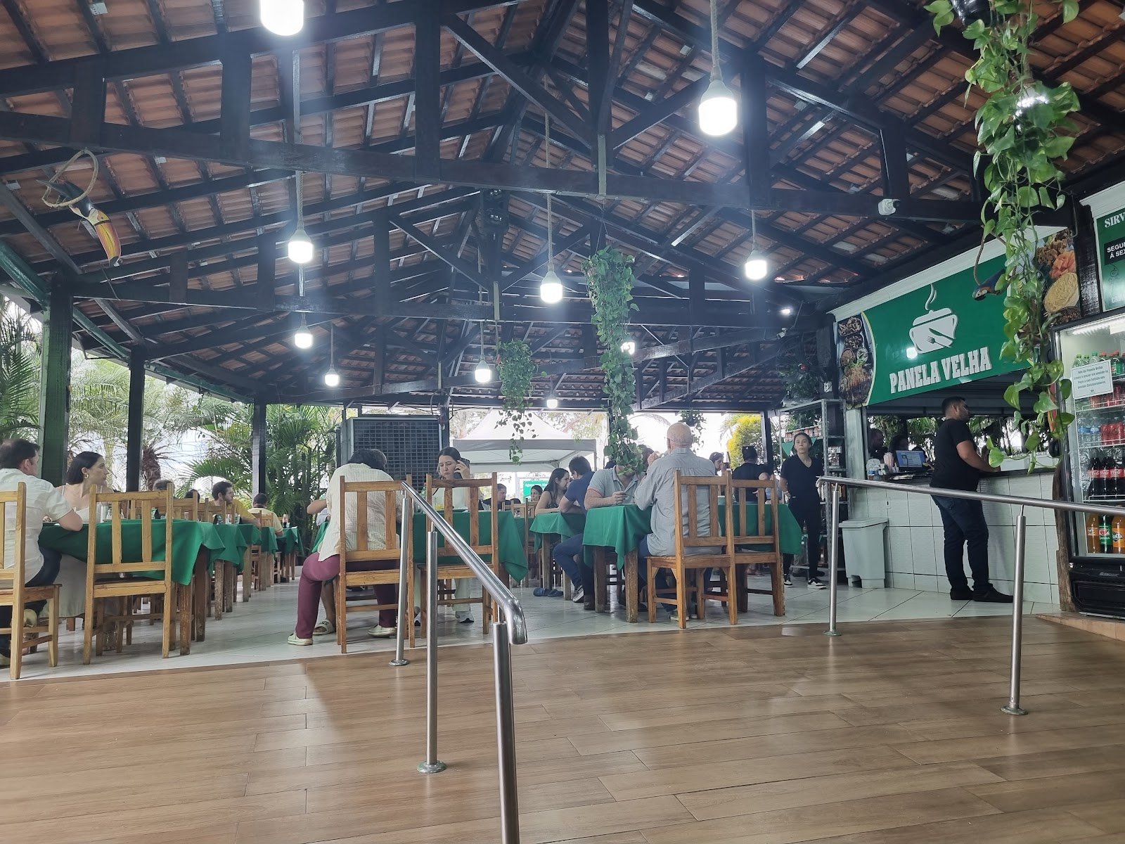 Salão coberto de madeira com clientes almoçando e a placa Panela Velha