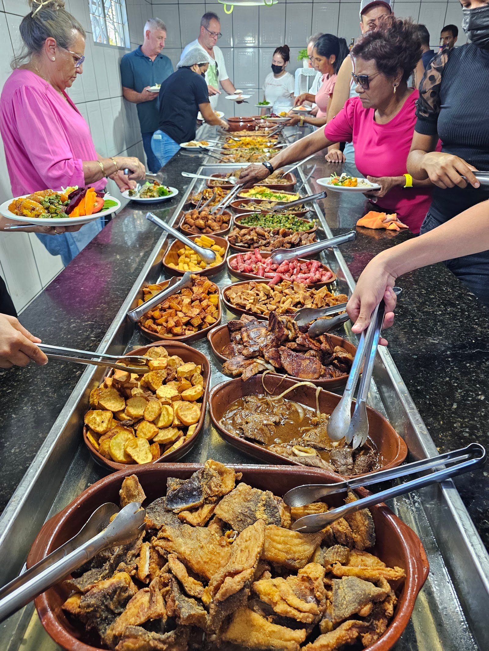 Fila do buffet com dezenas de panelas de barro e clientes se servindo